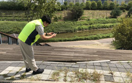 형광 조끼를 착용한 남성이 야외에서 인도 바닥 상태를 촬영하며 안전점검 중인 모습.